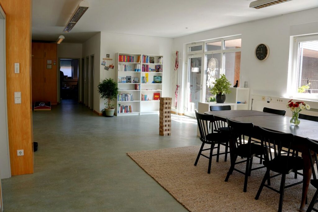 Weiter Blick durch den Aufenthaltsraum mit Bücherwand und Tisch