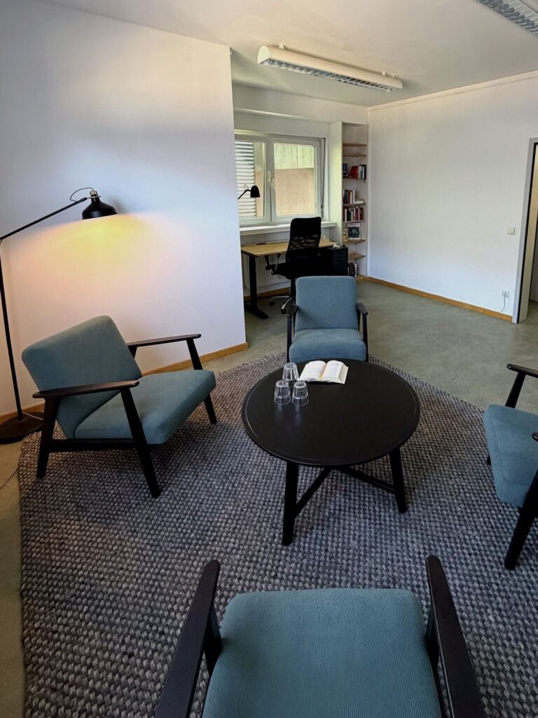 Beratungs- und Therapieraum mit Sesselrunde, Couchtisch und Arbeitsplatz am Fenster